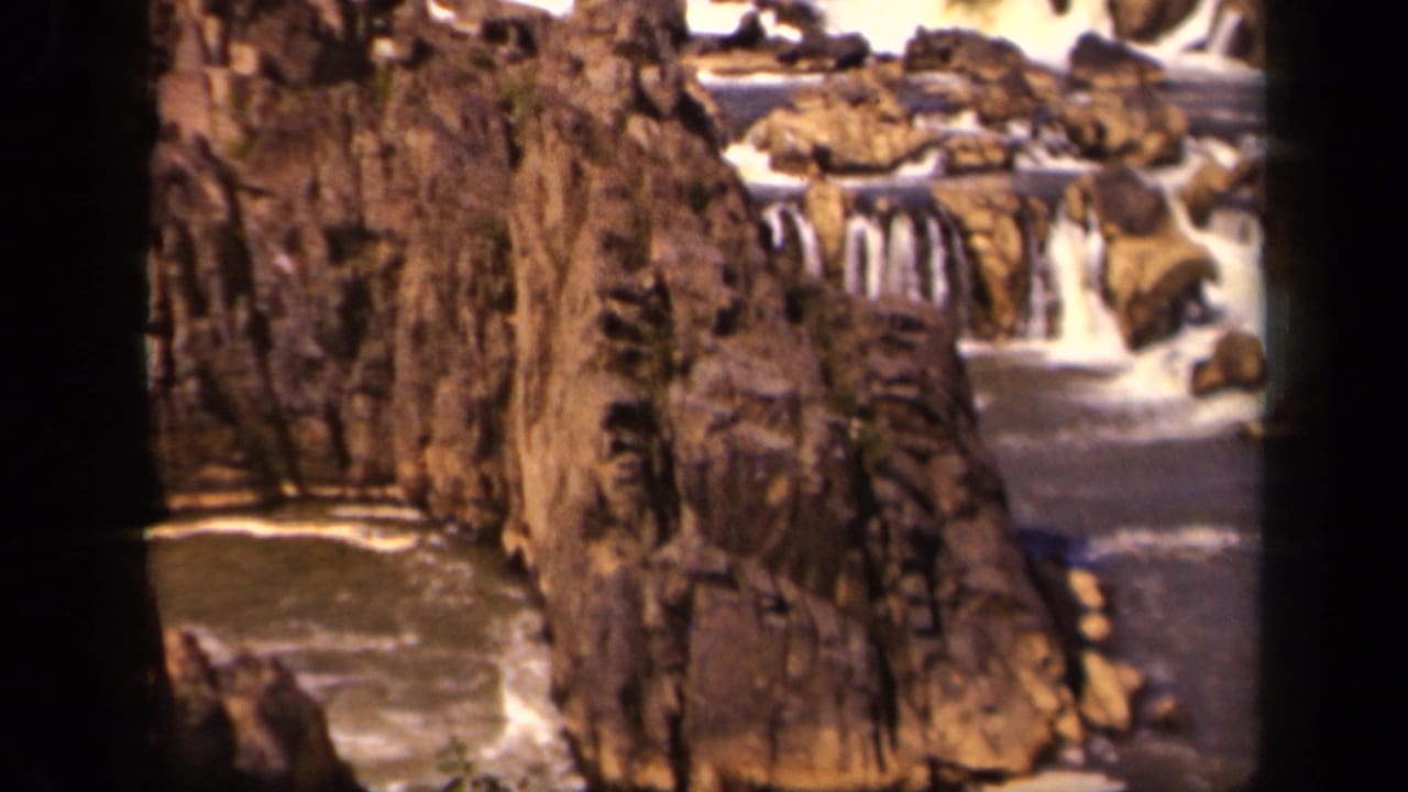 1943 8mm home-movie frame showing a rocky waterfall channel in the Baltimore, Maryland area, with brown cliff faces and white water.