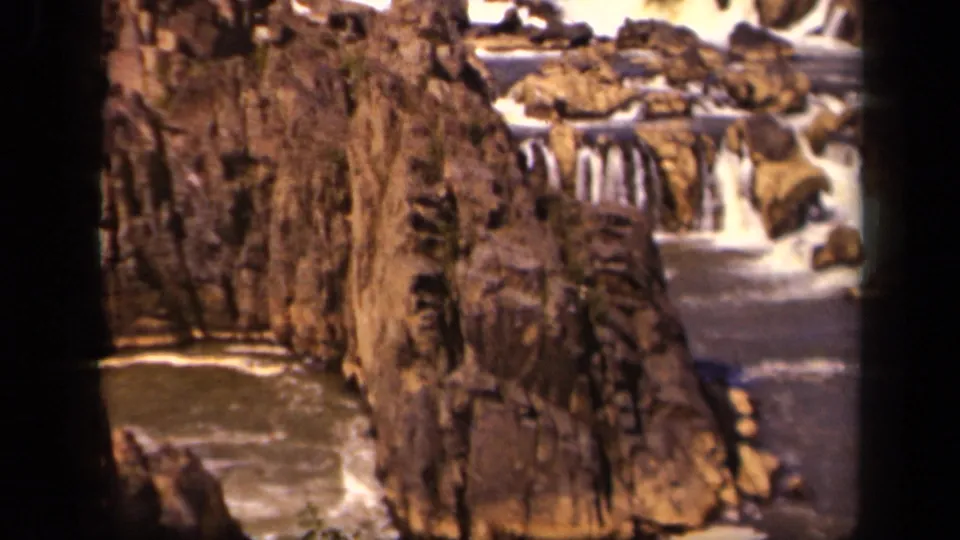 1943 8mm home-movie frame showing a rocky waterfall channel in the Baltimore, Maryland area, with brown cliff faces and white water.