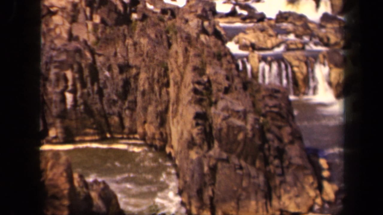 Brown rock face beside small cascades and moving water.