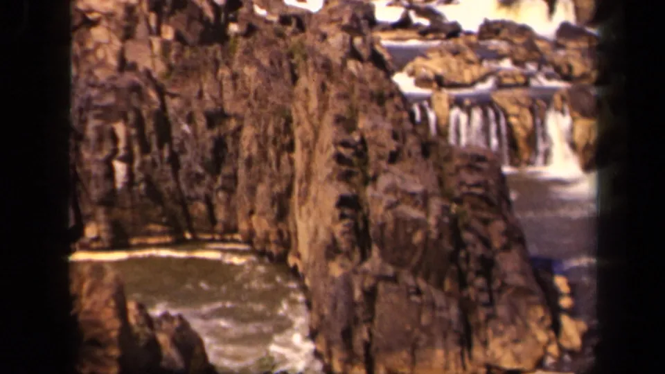 1943 8mm frame of rugged brown rocks and small cascades, with the water partly framed by dark film edges.