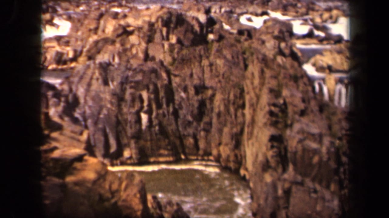 1943 8mm home-movie frame of a rocky gorge in the Baltimore metadata area, with a stream and small falls below weathered cliffs.