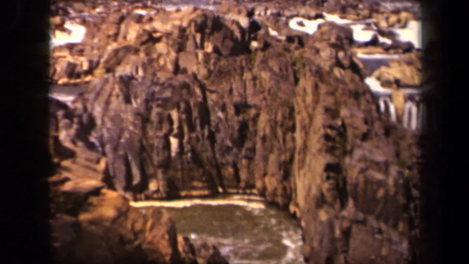 1943 8mm home-movie frame of a rocky gorge in the Baltimore metadata area, with a stream and small falls below weathered cliffs.
