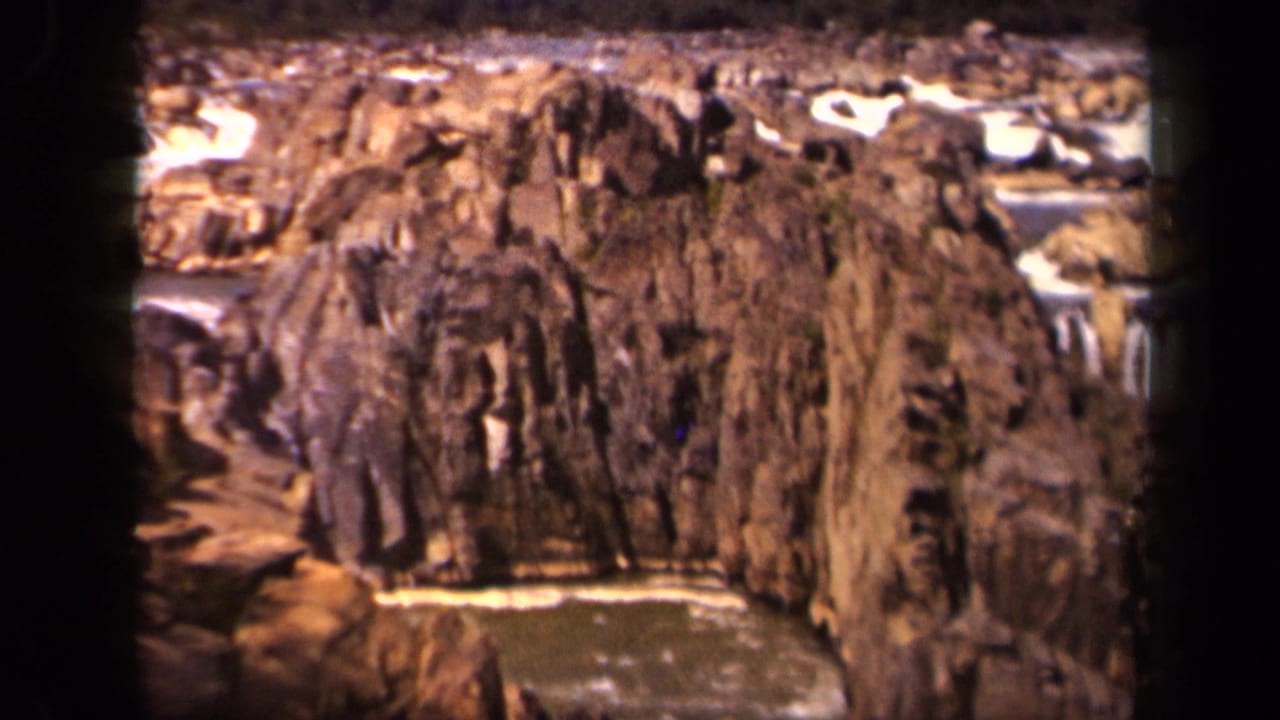 Rocky gorge with water flowing below steep brown cliffs.