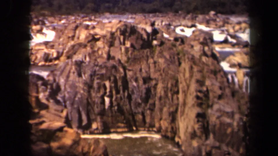 Archival home-movie frame of weathered canyon rock with a narrow stream and pale water highlights at the base.