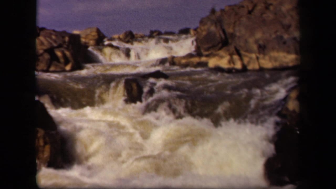 Foaming water rushes over dark rocks in a rocky channel.