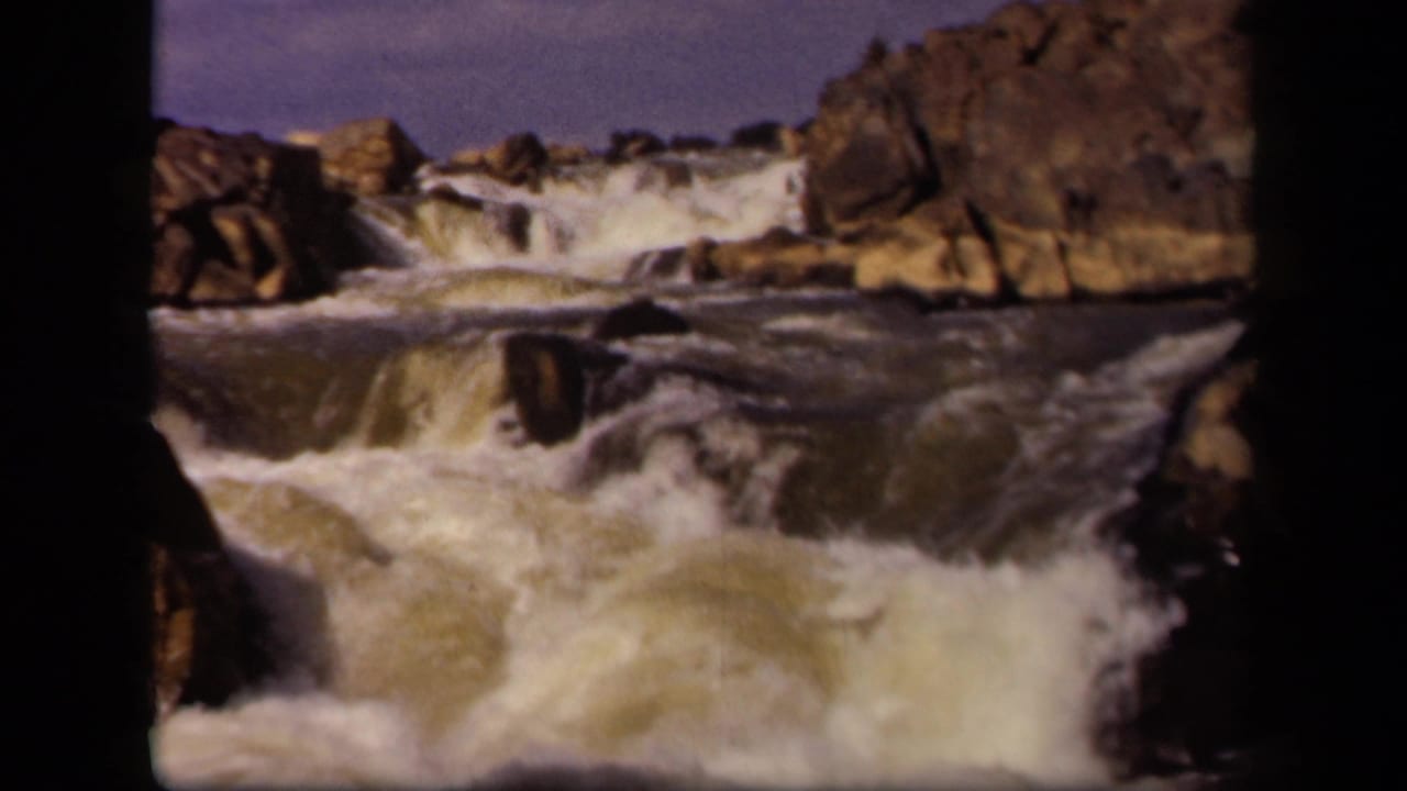 Rapids churn around boulders with white spray in the foreground.