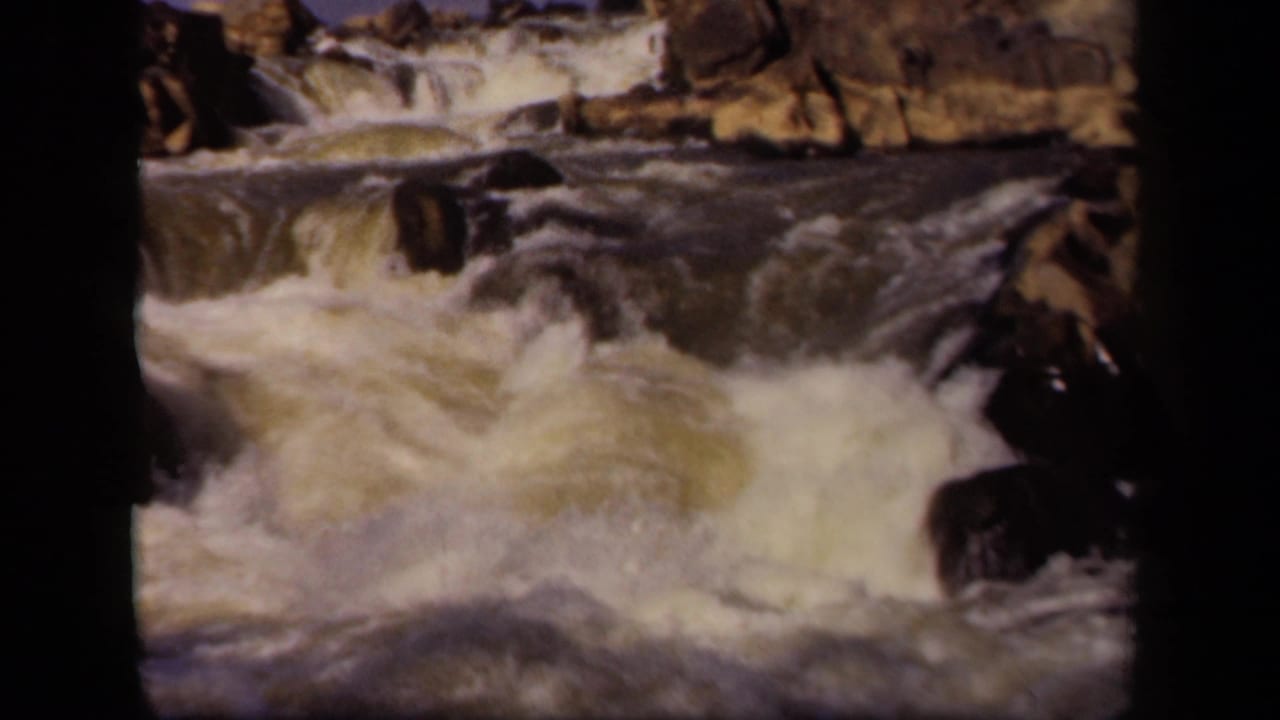 1943 Baltimore-area 8mm frame showing turbulent whitewater cascading across dark rocks, with a rocky ledge near the top.