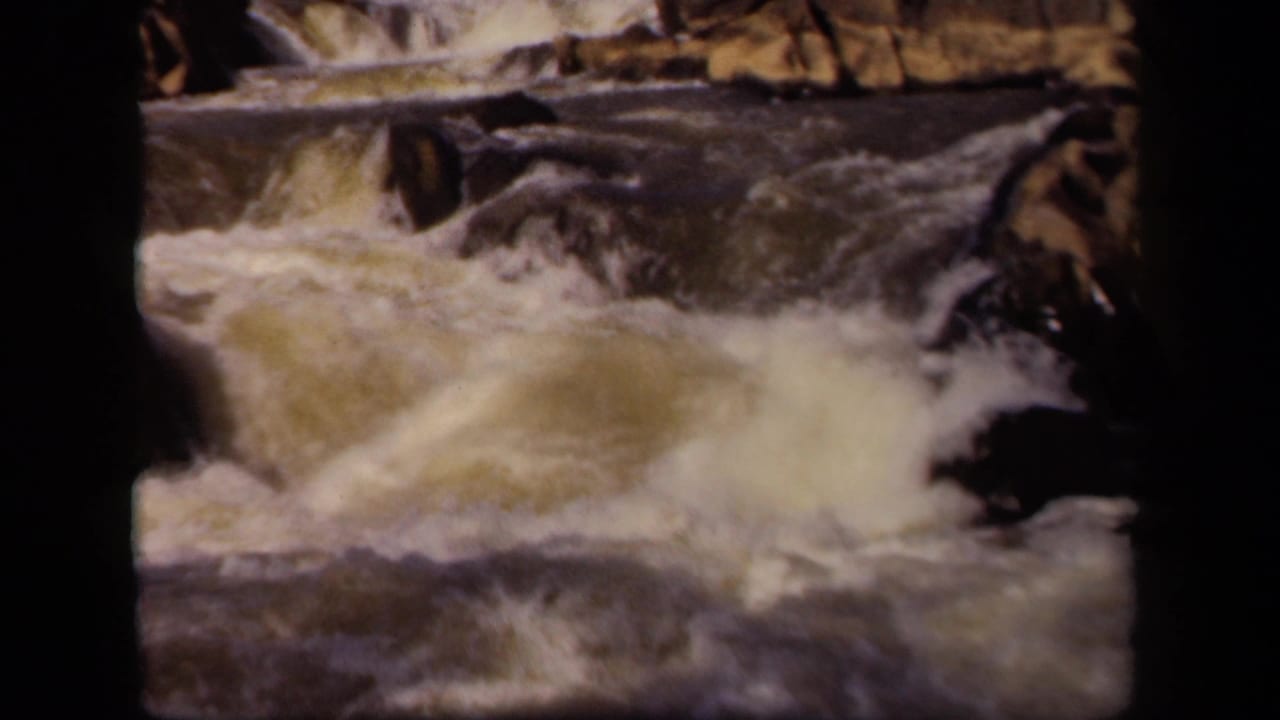 Rapids surge around rocks with frothy water filling the center of the frame.