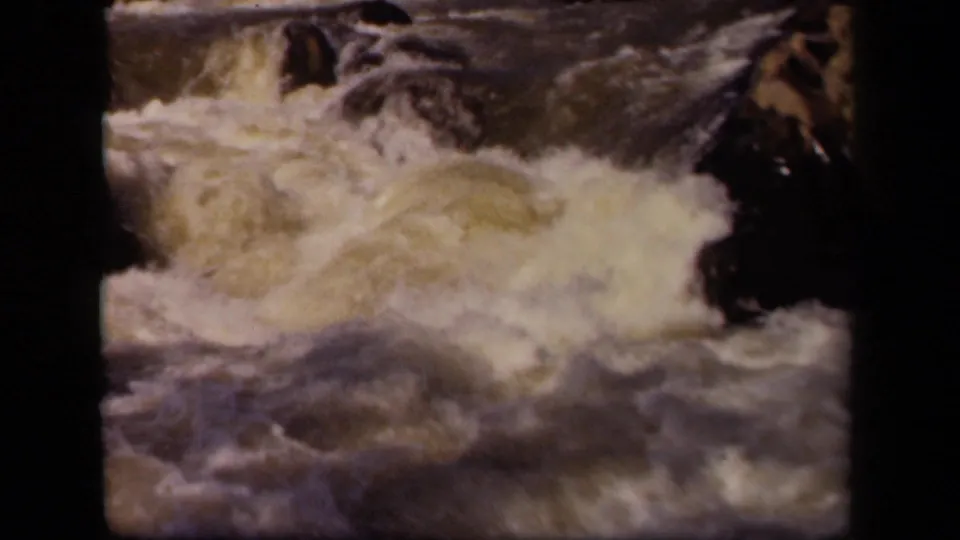 1943 Baltimore-area 8mm frame showing a closer burst of whitewater, dark rocks and a rough stone ledge.