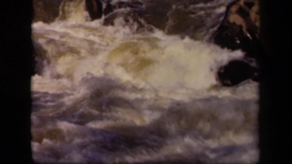 1943 Baltimore-area 8mm frame showing a broad foamy wave crossing a rocky streambed with dark frame edges.