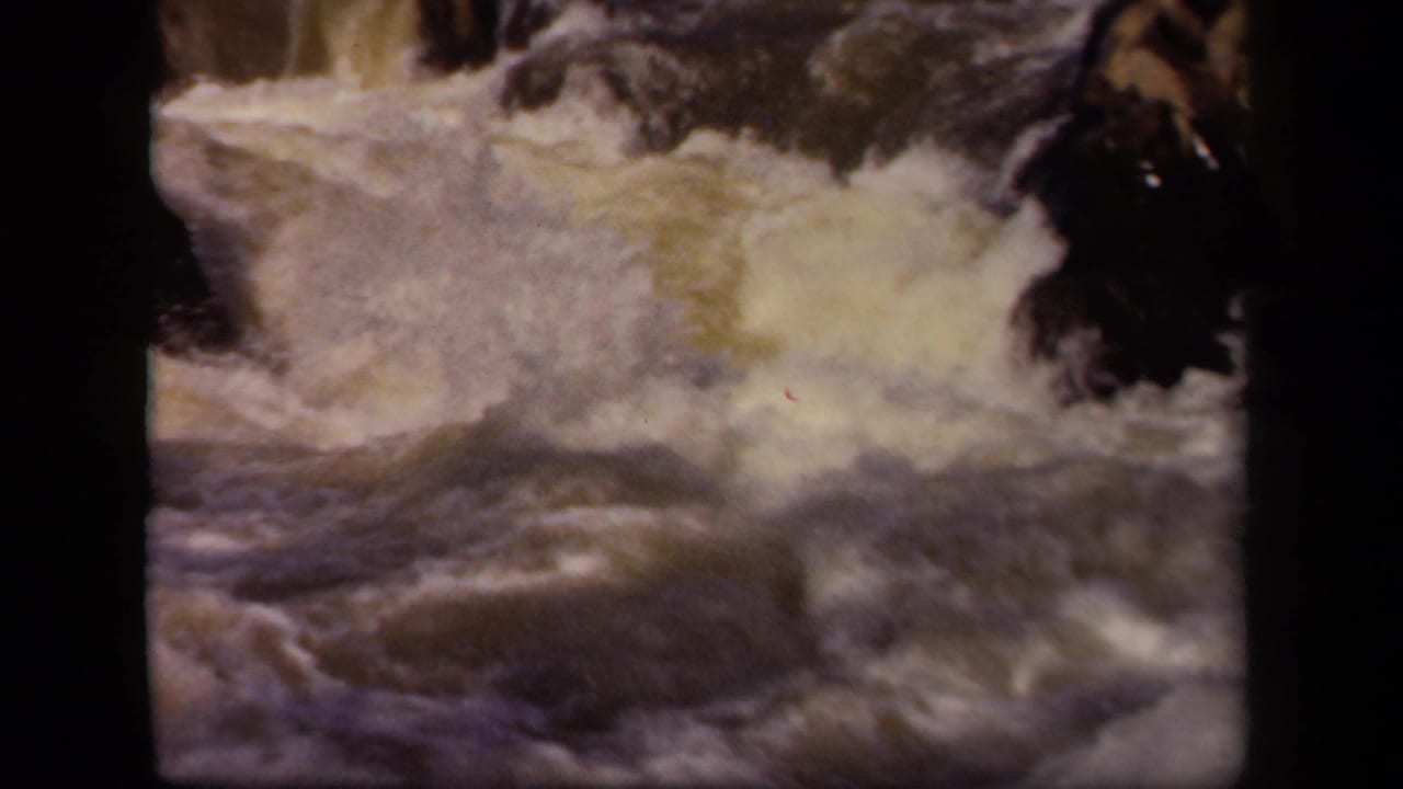 Foamy river water rushing over dark rocks in a vintage film frame.