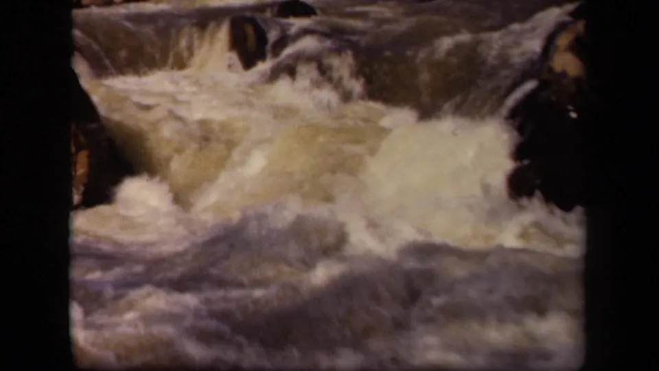 Close 8mm view of a rocky river rapid, with pale foam and turbulent water filling the frame.