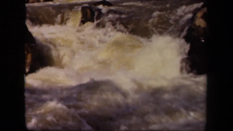 Vintage 8mm frame of turbulent river water surging through rocks, with soft motion blur and visible film texture.
