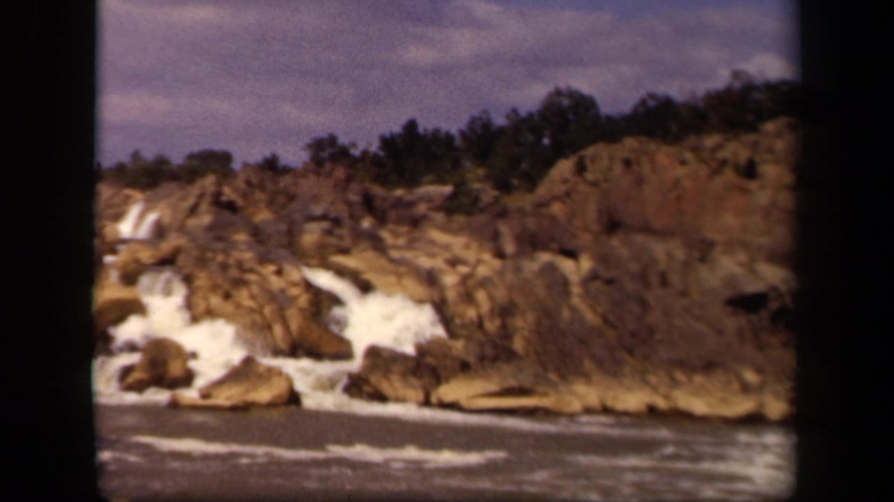 Rocky river ledge with white water spilling through jagged terrain under a cloudy sky.