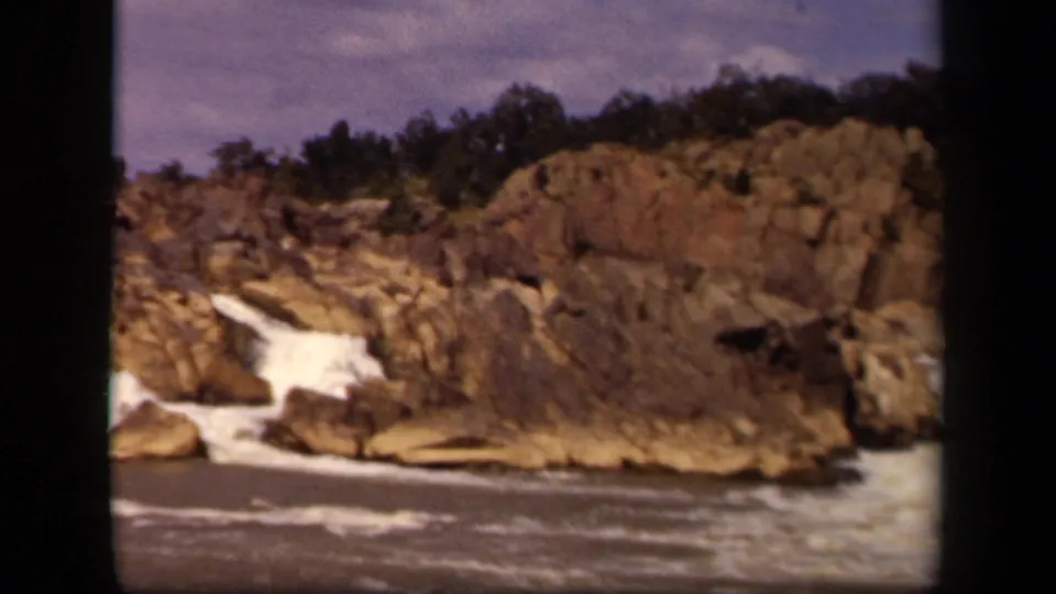 1943 Baltimore-associated 8mm frame showing a small cascade, foamy water, and a rugged rock wall with trees above.