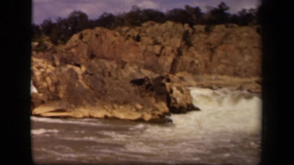 1943 Baltimore-associated home-movie frame showing foamy water at the base of jagged rocks and a dark tree line.