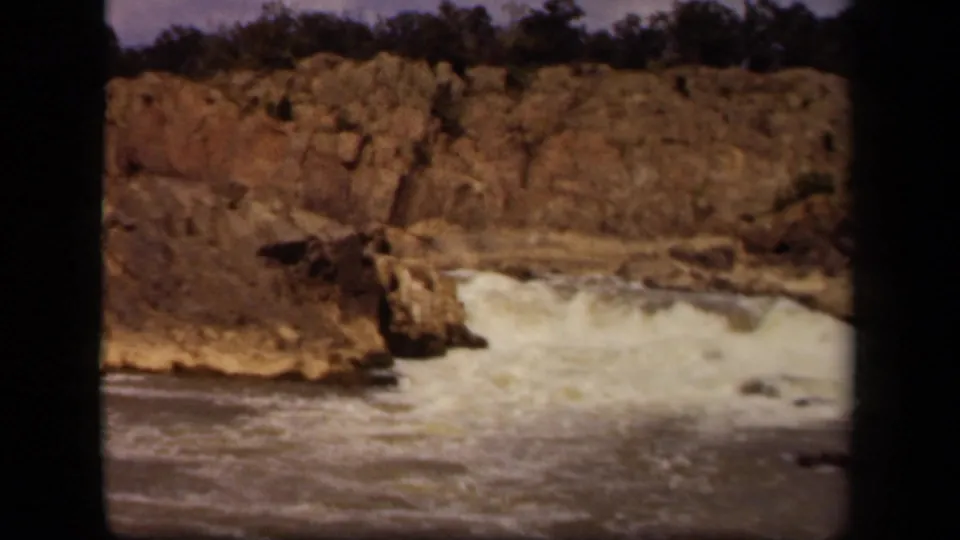 1943 Baltimore-area 8mm frame showing foaming water moving over low rocks beneath a rugged cliff line.
