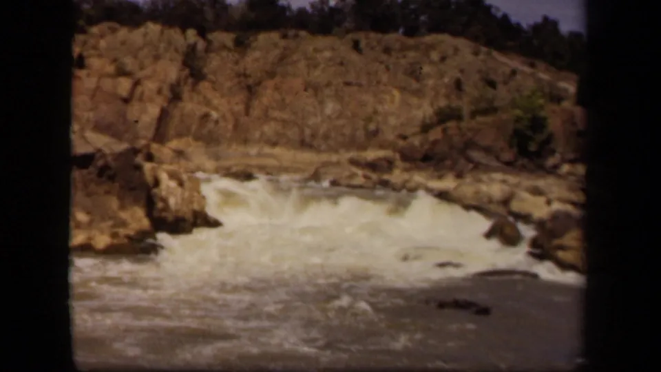 1943 8mm home-movie frame near Baltimore showing a white cascade moving through rocks below a tree-lined cliff.