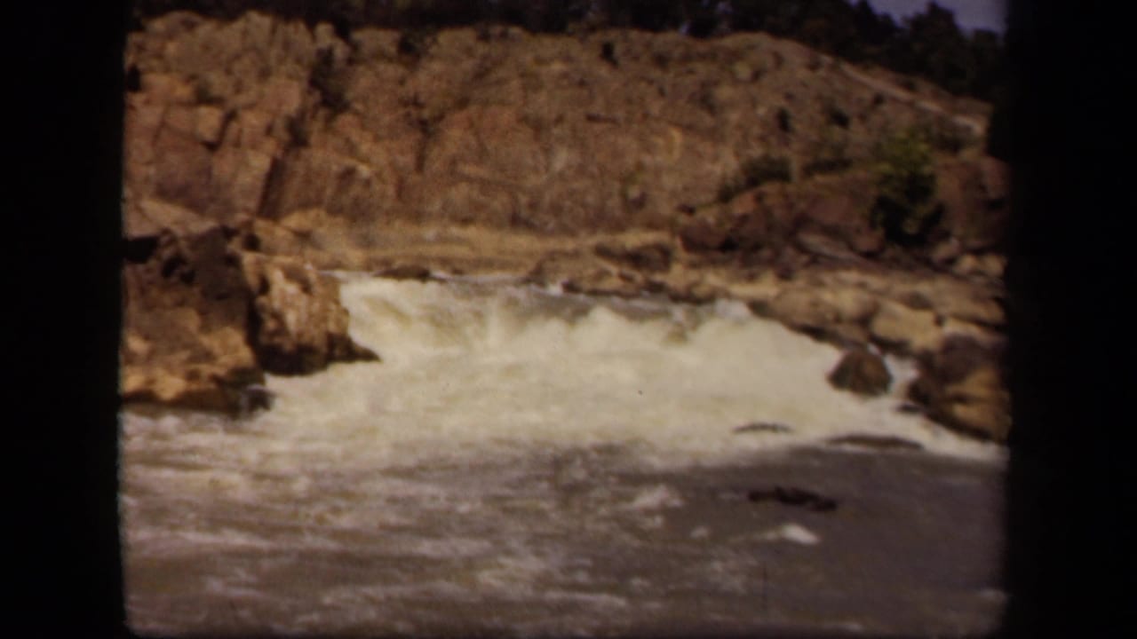 1943 Baltimore home-movie frame showing white water moving over rocky terrain, with soft focus and dark film edges.
