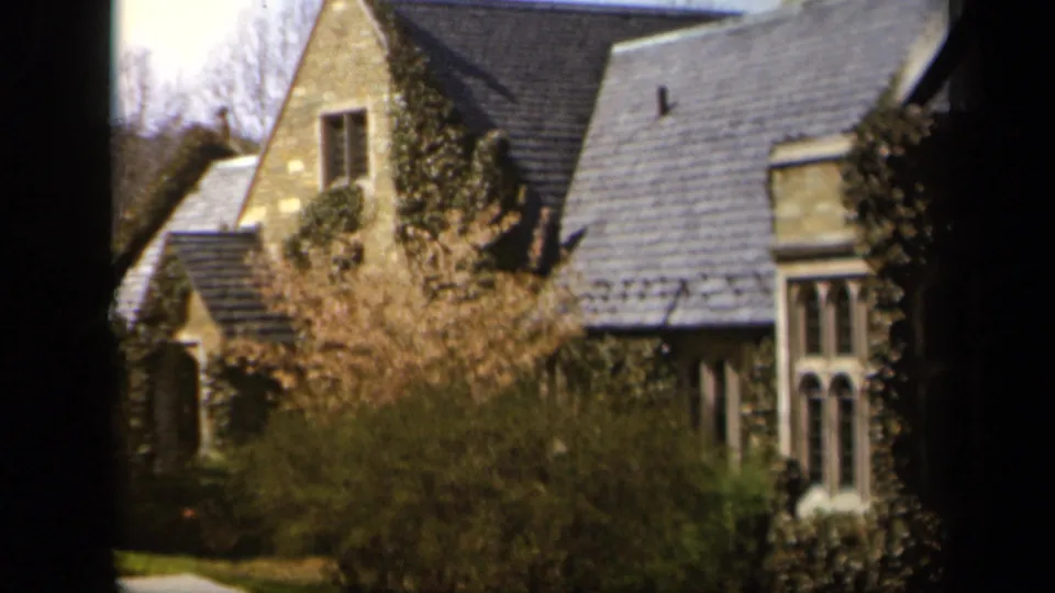 1943 Baltimore home-movie view of a stone residence, tall divided windows, dense shrubs, and a dark window-frame border.
