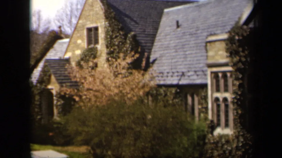 1943 Baltimore frame showing an ivy-covered stone house, roofline, shrubs, lawn, and dark foreground window framing.