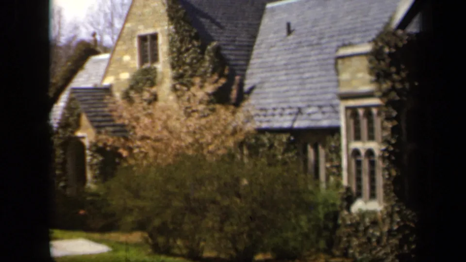 1943 Baltimore frame with a stone residential exterior, slate roof, ivy, shrubs, and pale spring blossoms across the foreground.