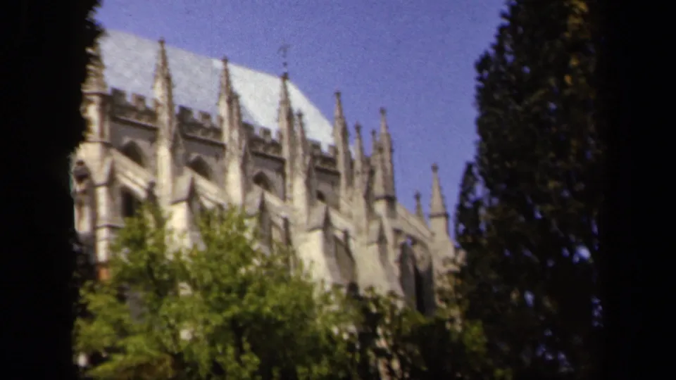 Brief 1943 home-movie view of a pale stone Gothic cathedral exterior framed by green trees and blue sky.