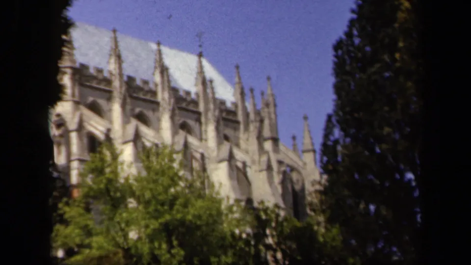 1943 Baltimore 8mm frame of a Gothic-style cathedral exterior partly framed by trees under blue sky.