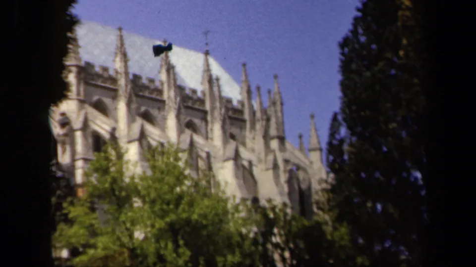 1943 Baltimore home-movie frame showing a Gothic cathedral exterior through trees, with a visible film artifact near the upper roof.