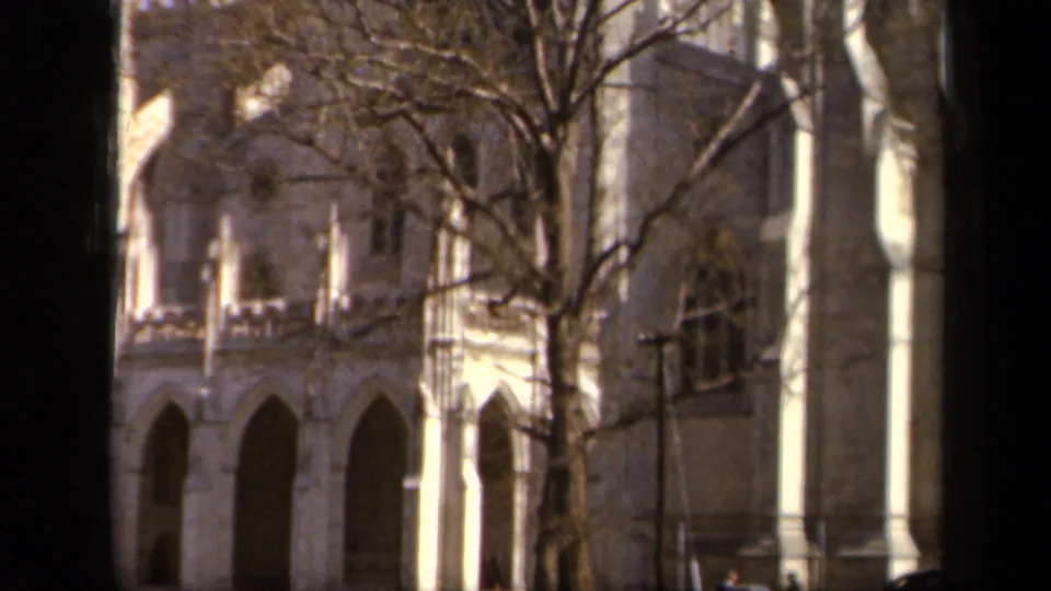 1943 Baltimore home-movie frame showing arched stone architecture behind bare trees, with small pedestrians near the lawn.