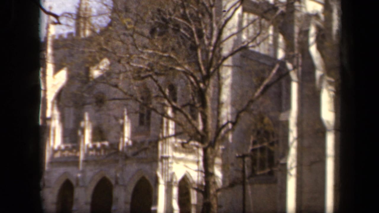 1943 Baltimore home-movie frame showing a pale stone Gothic-style facade with pointed arches and leafless branches in front.