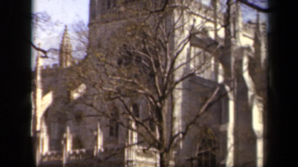 1943 Baltimore 8mm frame showing an upward pan across stone arches, deep windows, and bare branches on a historic-looking exterior.