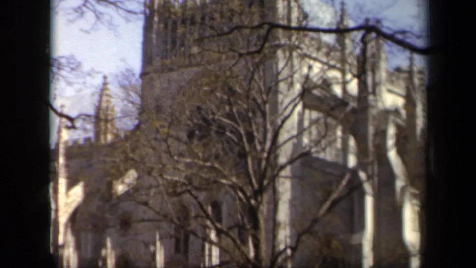 Final 1943 Baltimore frame with a tall Gothic-style stone tower, arched openings, and bare branches crossing the exterior.