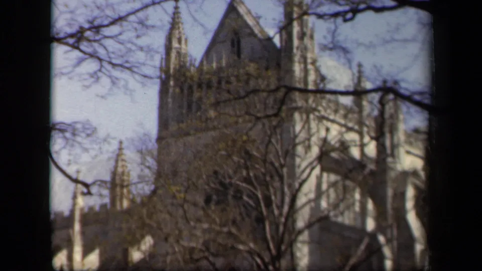 1943 Baltimore 8mm still of a pale stone Gothic-style church facade seen through dark branches.