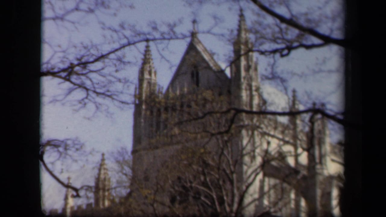 1943 Baltimore 8mm frame of a Gothic-style stone cathedral viewed through bare branches against a pale sky.