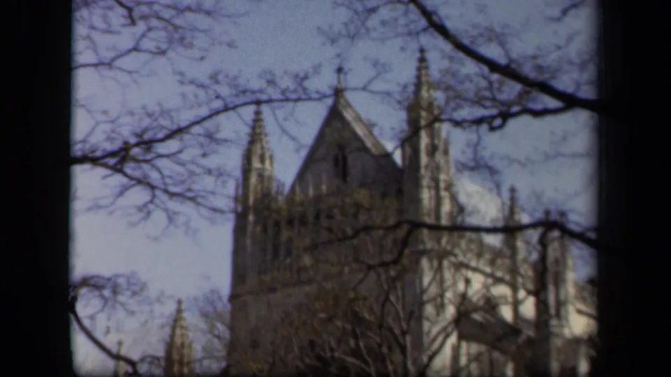 1940s Baltimore home-movie view of a Gothic cathedral facade, softened by grain and branches in the foreground.