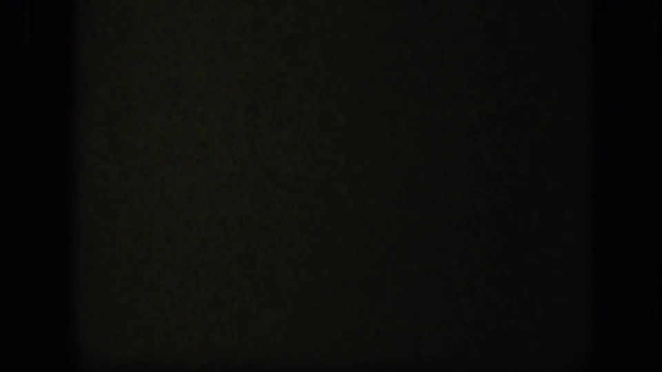 A near-black transitional frame with faint green texture and visible film grain from the 8mm scan.
