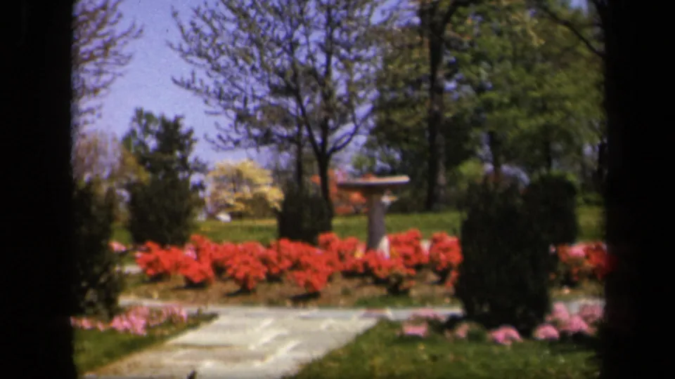The closing frame repeats the landscaped garden composition, with red blooms, a pale path, trees, lawn, and a stone bird bath under blue sky.