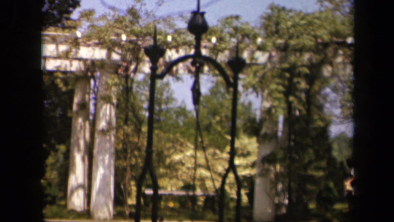White garden pillars and dark ironwork partly obscured by trees and shadow.