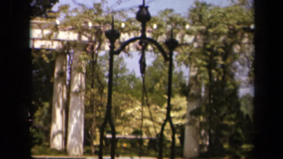Skyline Drive garden scene showing white pillars, dark ironwork, trees, and a bright 1940s home-movie color palette.
