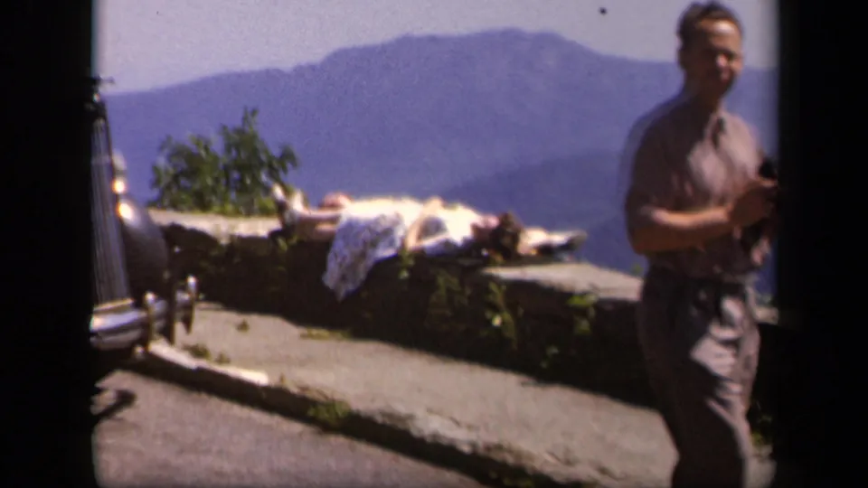 At the Virginia mountain overlook, a man appears at frame right while a woman sunbathes on the stone ledge below distant ridges.