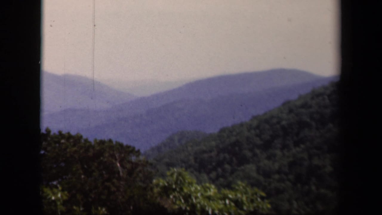 1943 Skyline Drive view with receding Blue Ridge-like mountain layers, foreground trees, and visible 8mm gate edges.