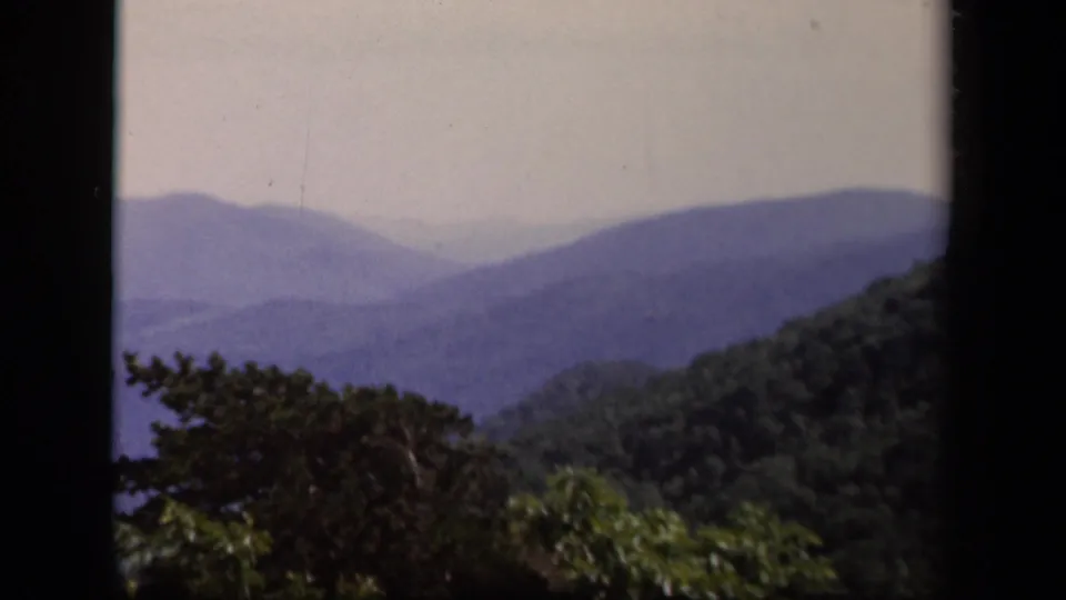 Home-movie overlook view from Skyline Drive, Virginia, with green foliage below layered blue mountains.