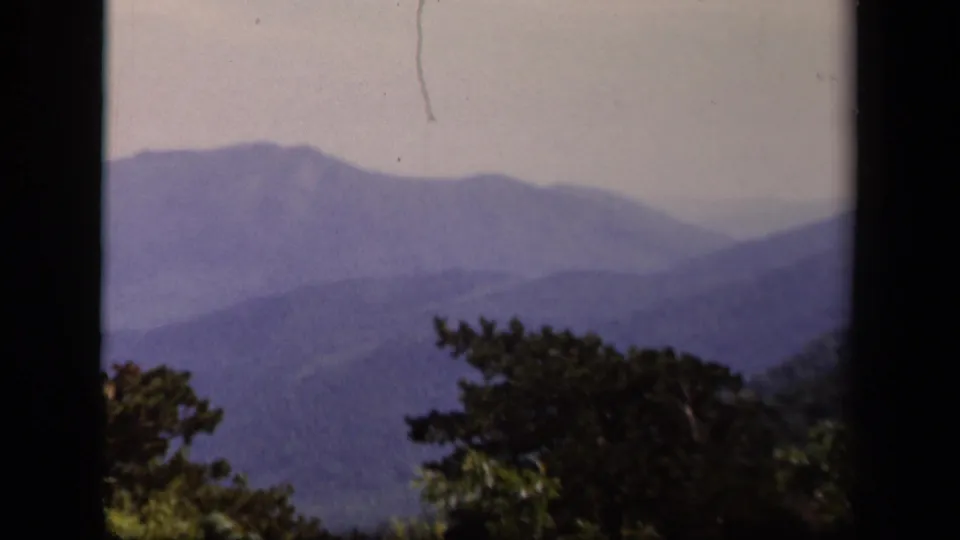 Skyline Drive home-movie still of blue-purple mountain layers, hazy sky, and dark evergreen-like treetops.