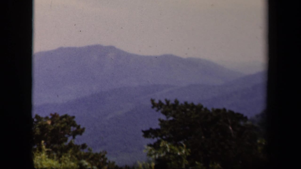 Blue mountain ridges seen through dark film-frame edges and tree silhouettes.