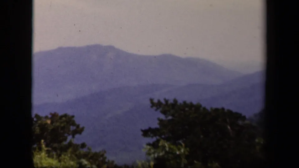 Layered blue ridges near Skyline Drive, Virginia, framed by dark 8mm gate edges and foreground trees.