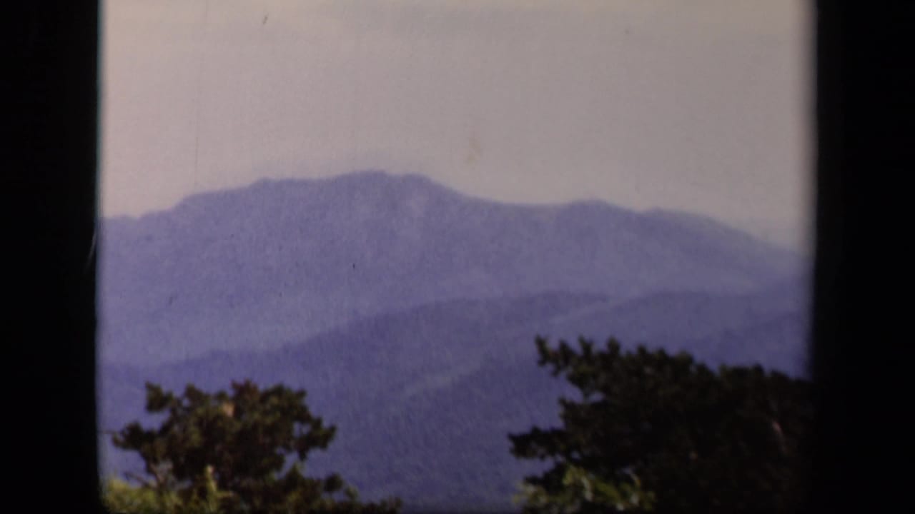 A hazy Skyline Drive mountain vista on 8mm film, with blue ridges, trees, and heavy frame-edge shadow.