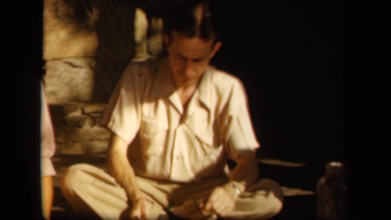 Adult man in a light shirt sits cross-legged near stone steps in shadow.