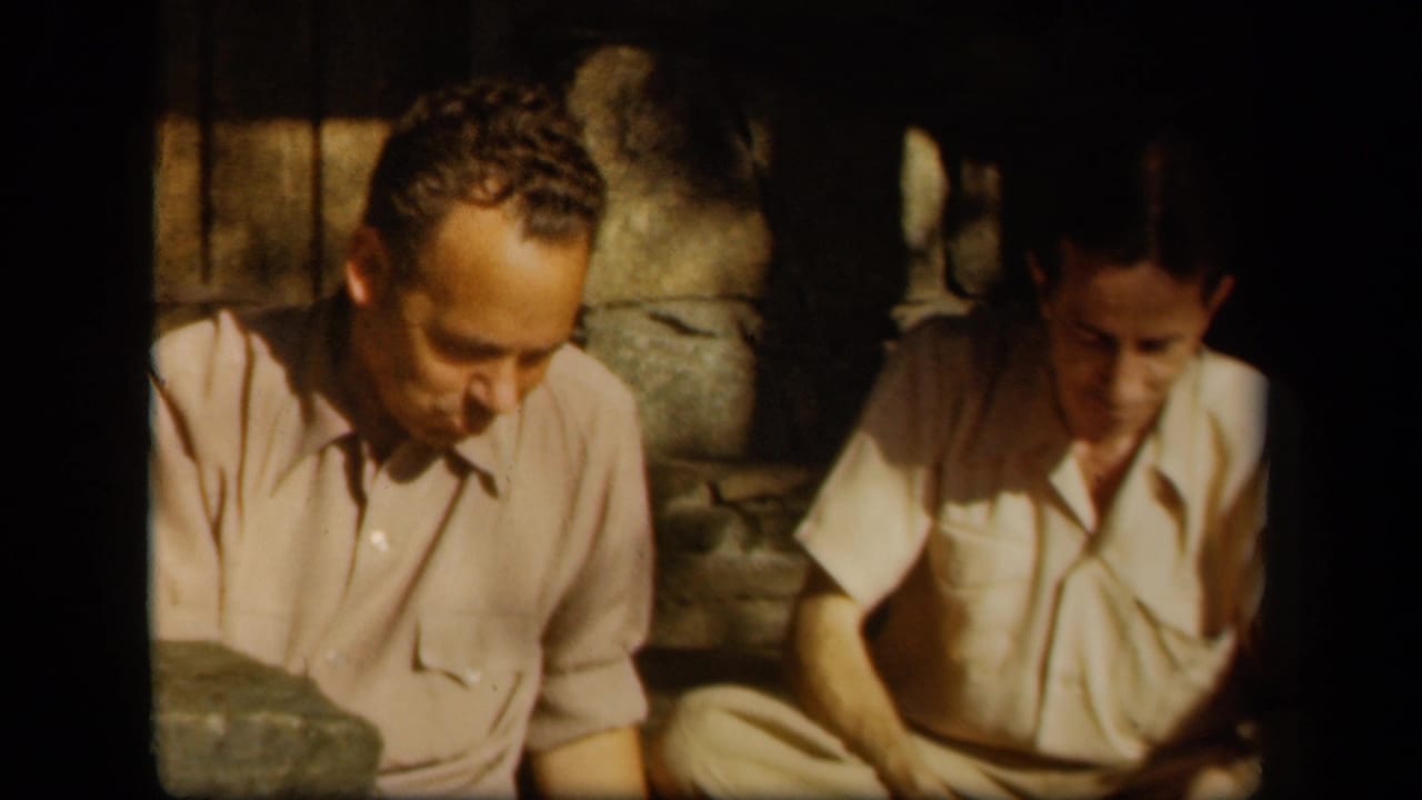 Two men remain seated in shadow, with one looking down while eating.
