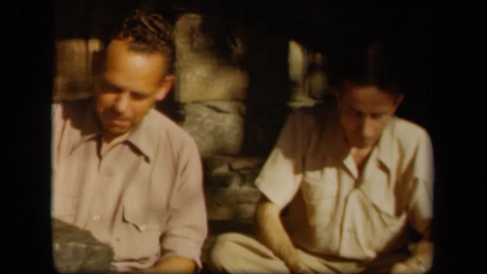 1943 Skyline Drive home-movie frame with two men seated near a stone wall, one partly cropped by the frame edge.